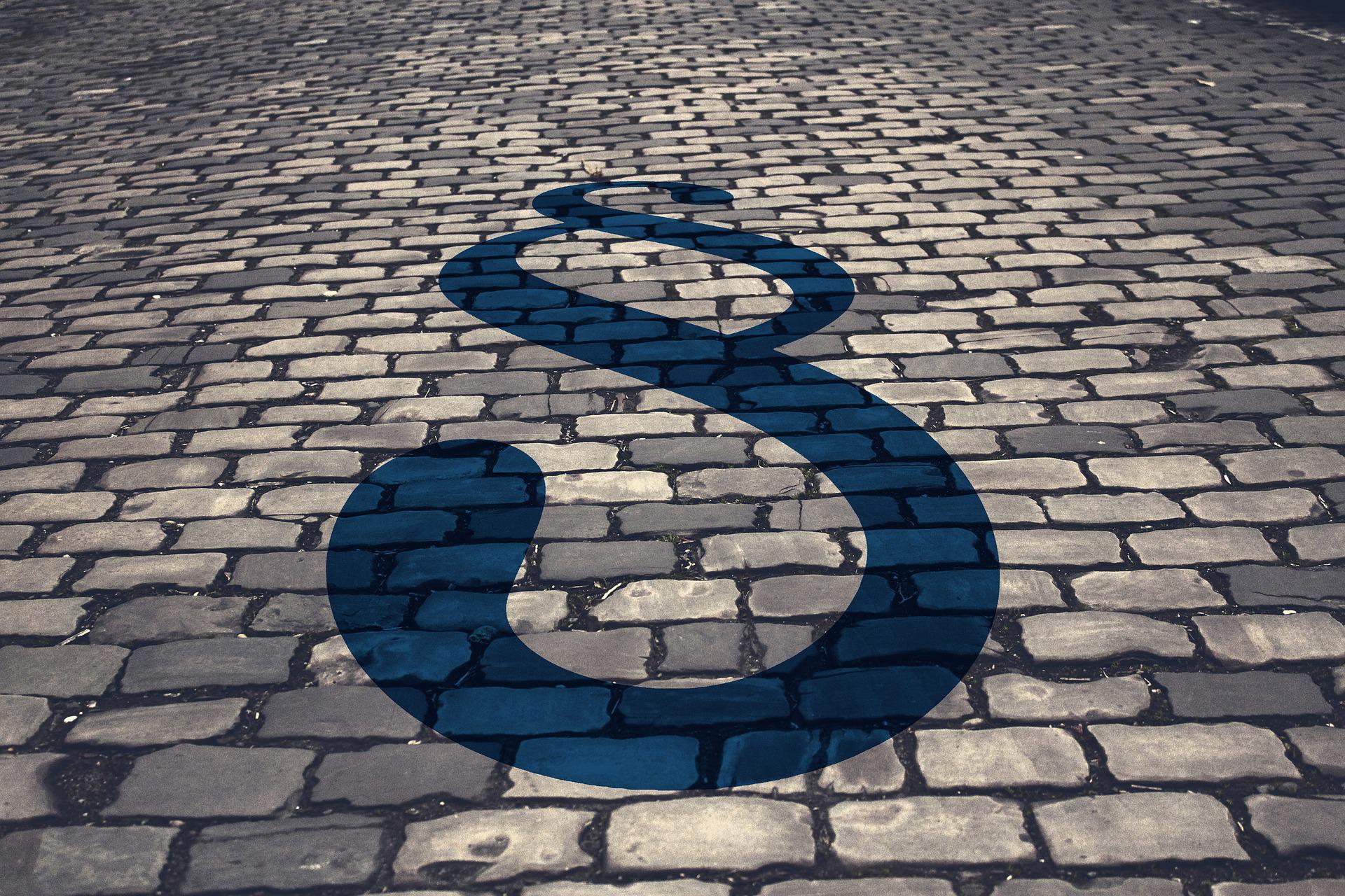 fragment drogi brukowanej, na niej czarny symbol graficzny paragrafu